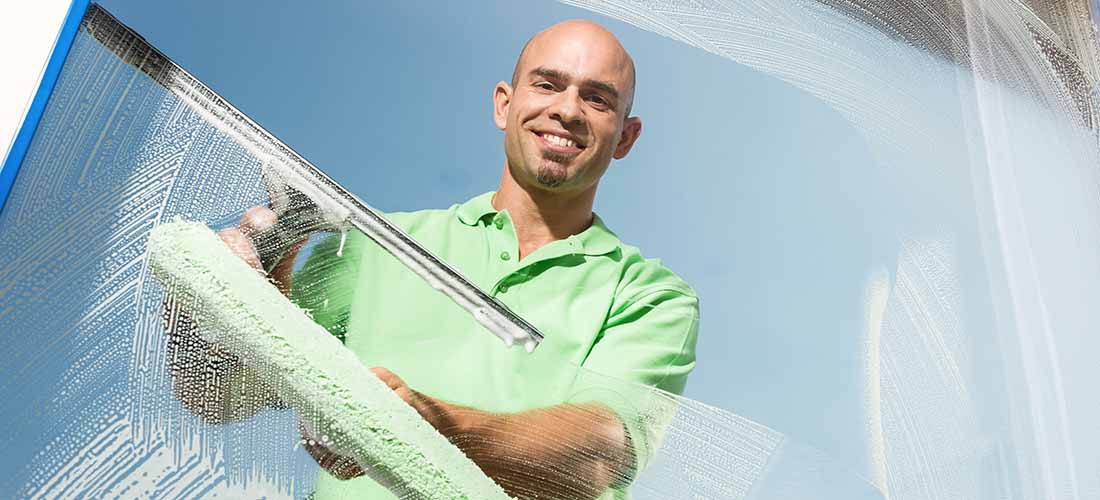 Hehl GmbH, Gebäudereinigung in Ludwigshafen: Fensterputzer in pastellgrünem T-Shirt lächelt durch klargewischte Scheibe
